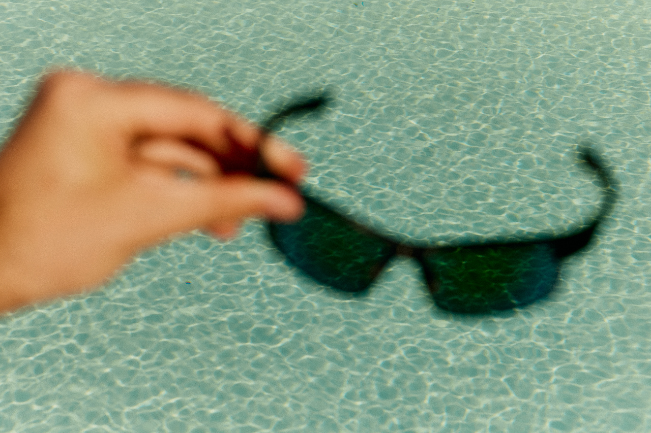 A hand holding sunglasses above a pool